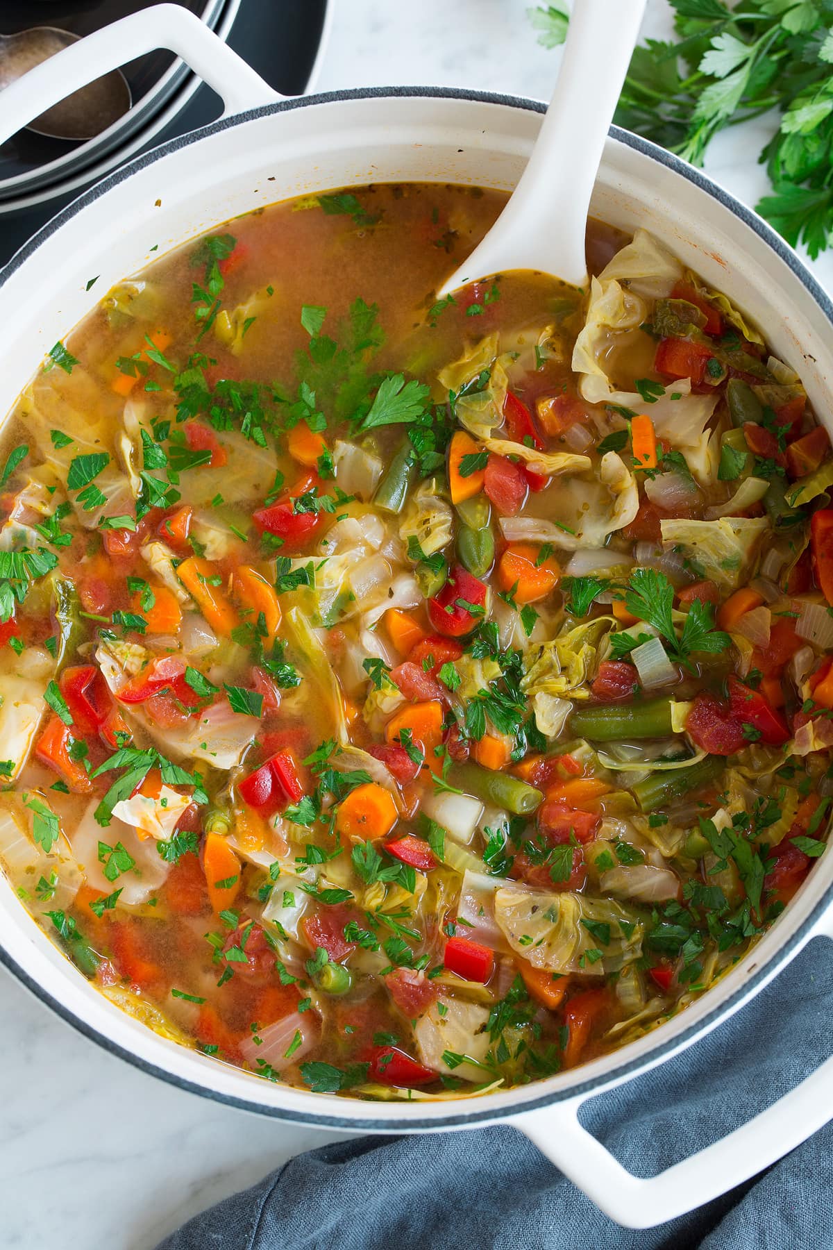 Cabbage Soup Overhead image of cabbage soup in a large white pot with a white ladle, showing an abundance of fresh vegetables.