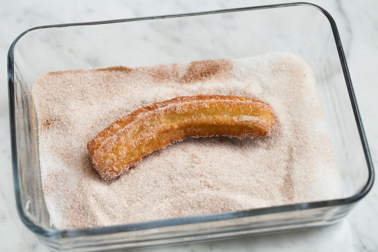churros rolling in cinnamon sugar mixture in dish
