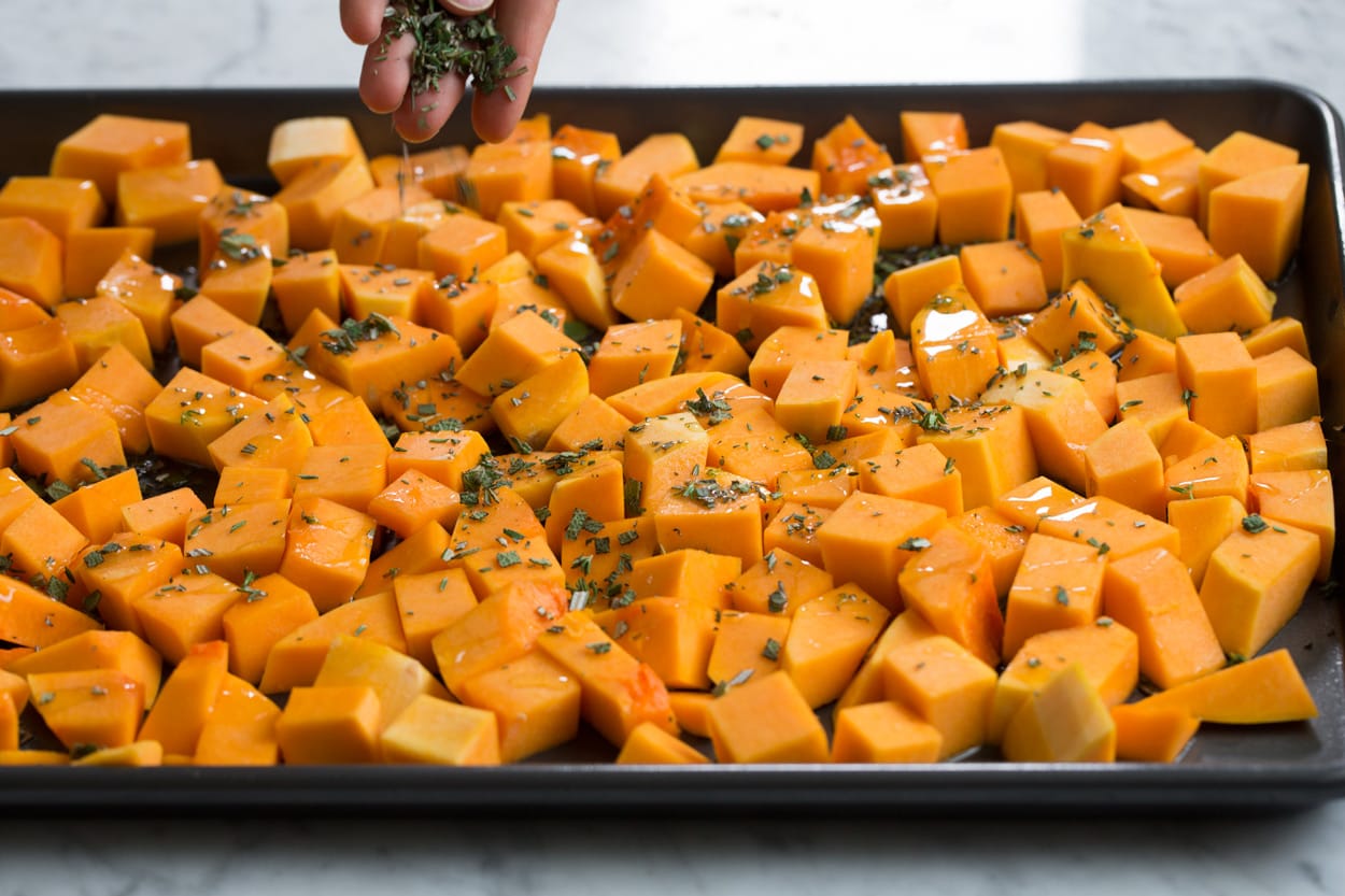 Roasted Butternut Squash with Garlic and Herbs Drizzling butternut squash on a baking sheet with olive oil and sprinkling with herbs.