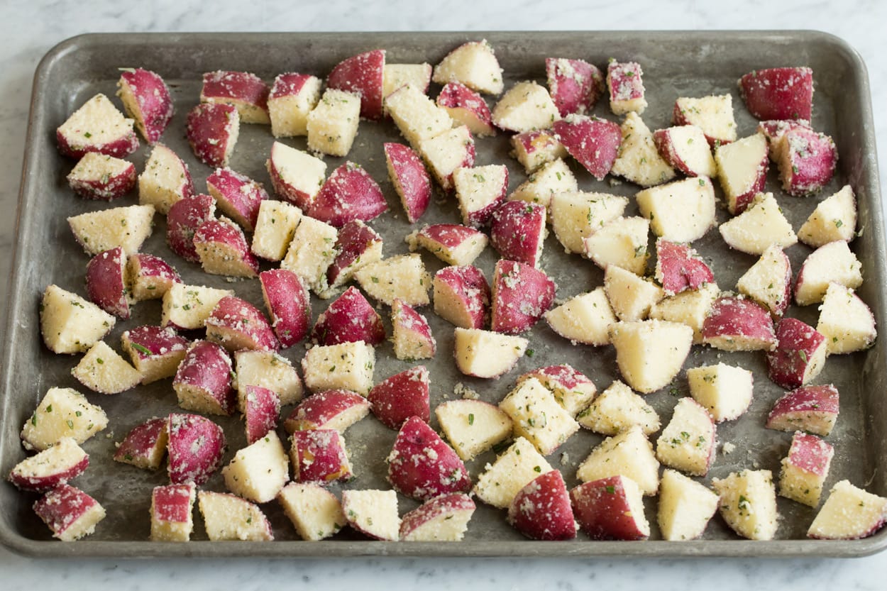 Roasted Potatoes with Parmesan Garlic and Herbs Potato cubes tossed with parmesan on a baking sheet to roast.