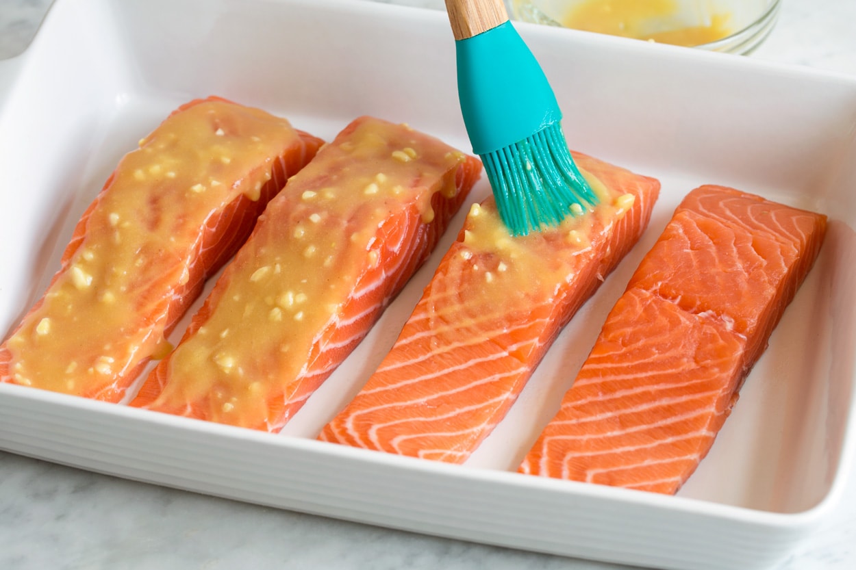 Baked Salmon with Buttery Honey Mustard Sauce Showing how to make baked salmon. Brushing four fillets in baking dish with honey mustard sauce.