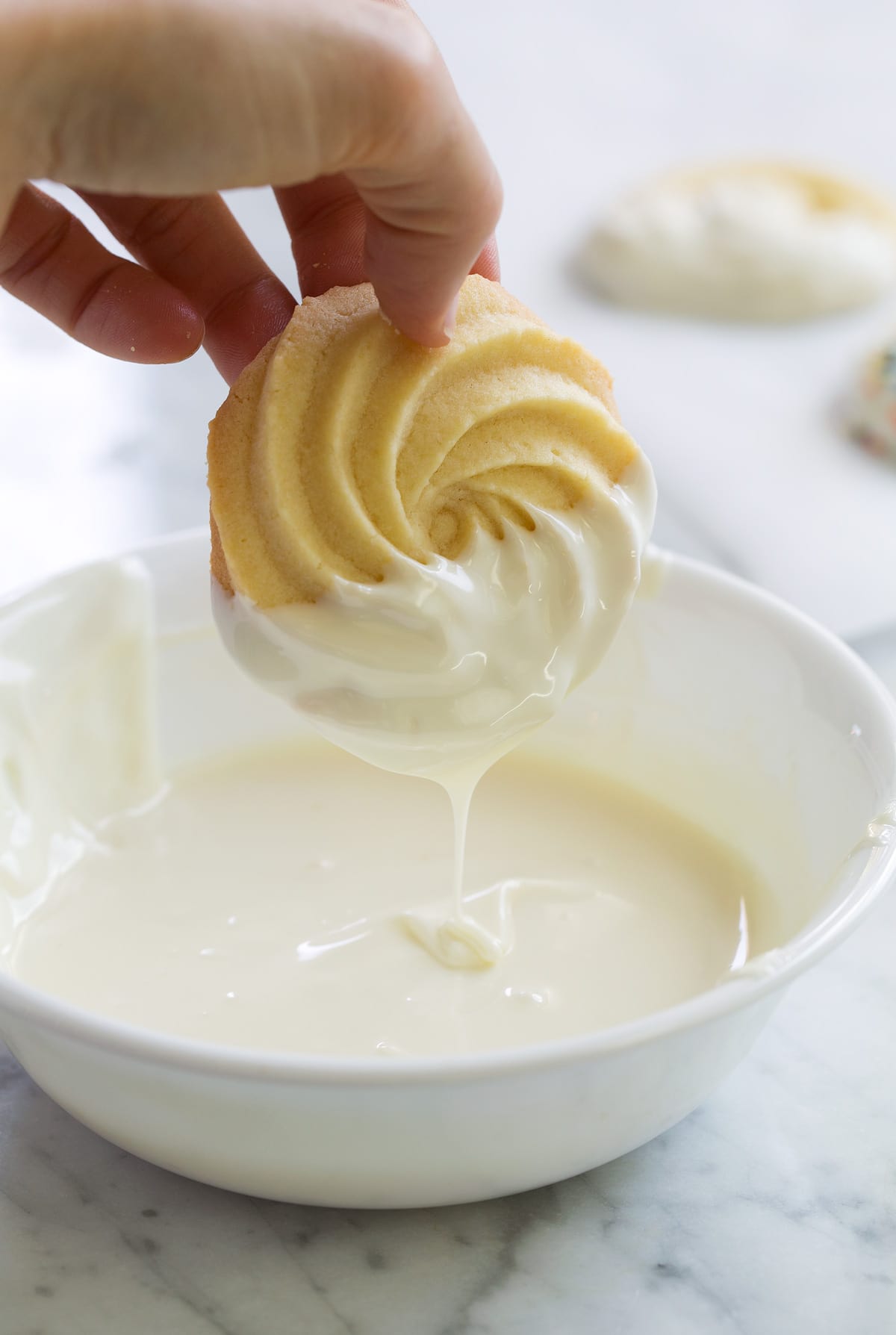 Butter Cookies Dipping butter cookie in white chocolate melts in a small bowl.