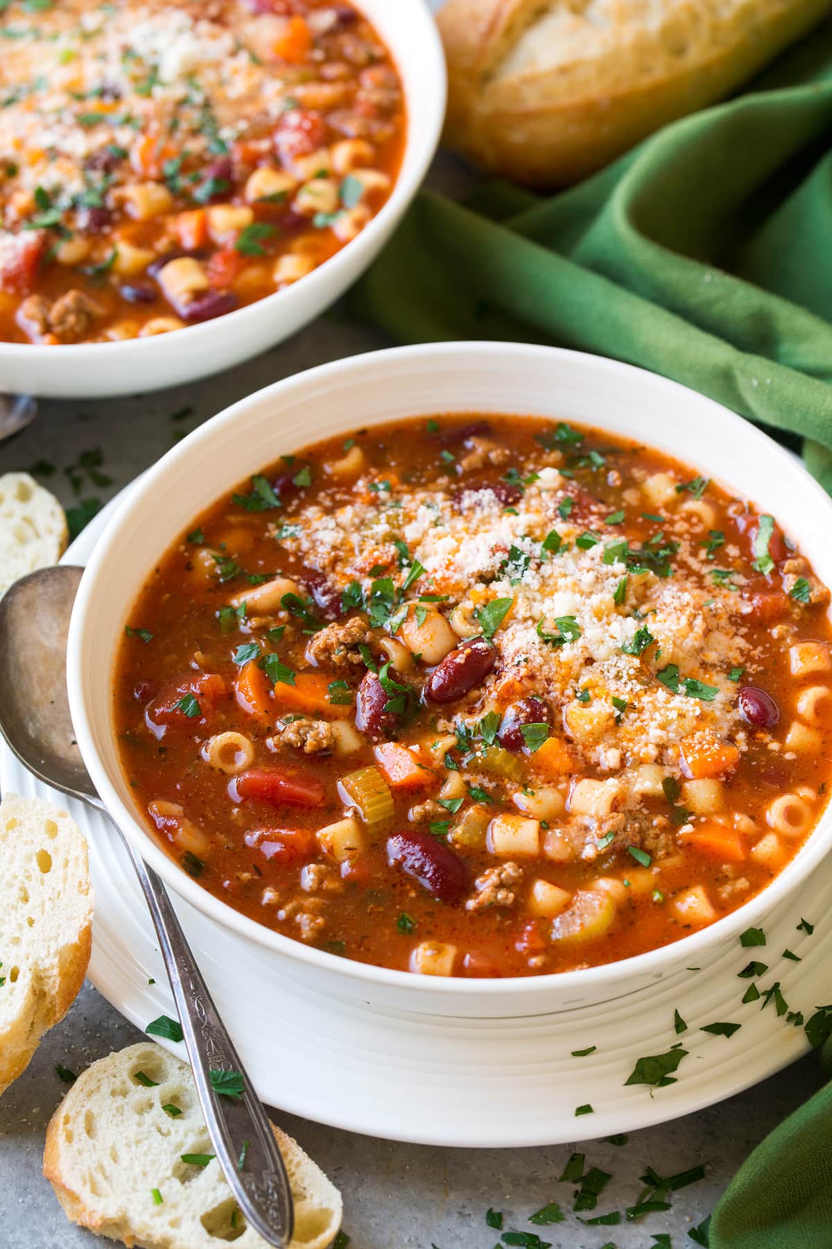The BEST Pasta e Fagioli Soup Recipe! Two servings of Pasta e Fagioli Soup in white serving bowls set over white plates. Served with french bread on the side.