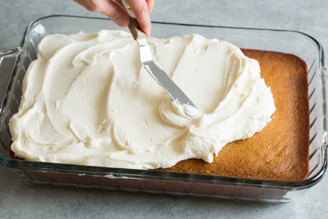 Pumpkin Cake shown here spreading cream cheese frosting onto pumpkin cake
