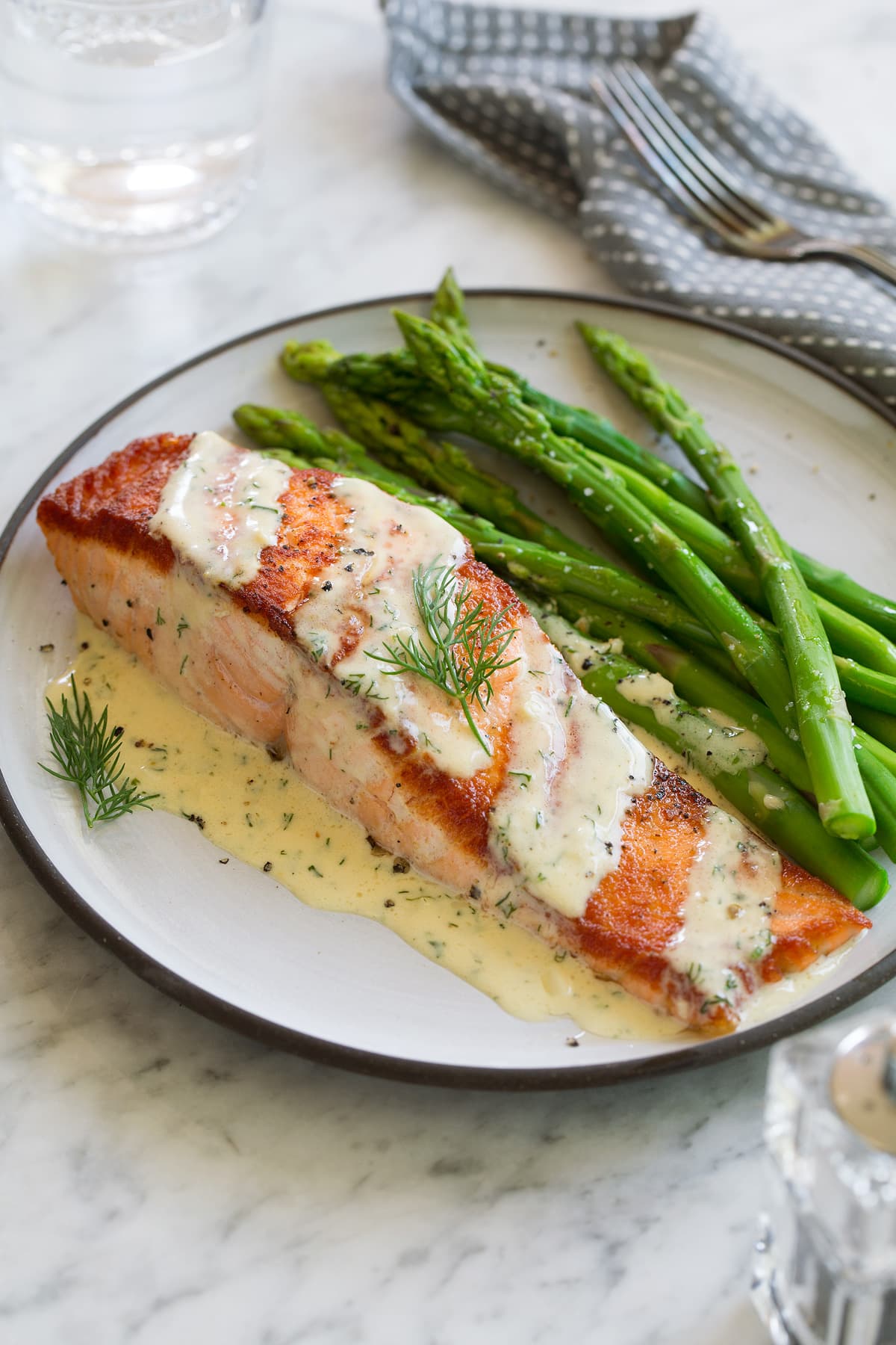 Salmon with Creamy Garlic Dijon Sauce Salmon fillet on a white plate set over a marble surface. Topped with dijon sauce and served with a side of asparagus.