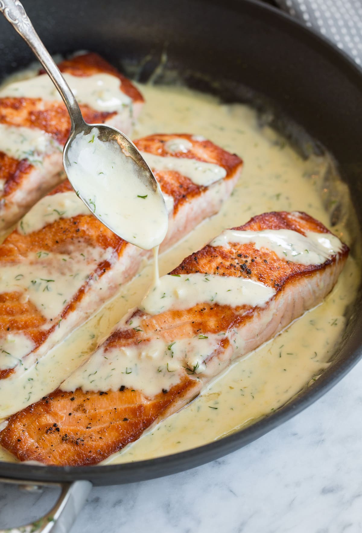 Salmon with Creamy Garlic Dijon Sauce Spooning sauce over a fillet of salmon in a skillet.