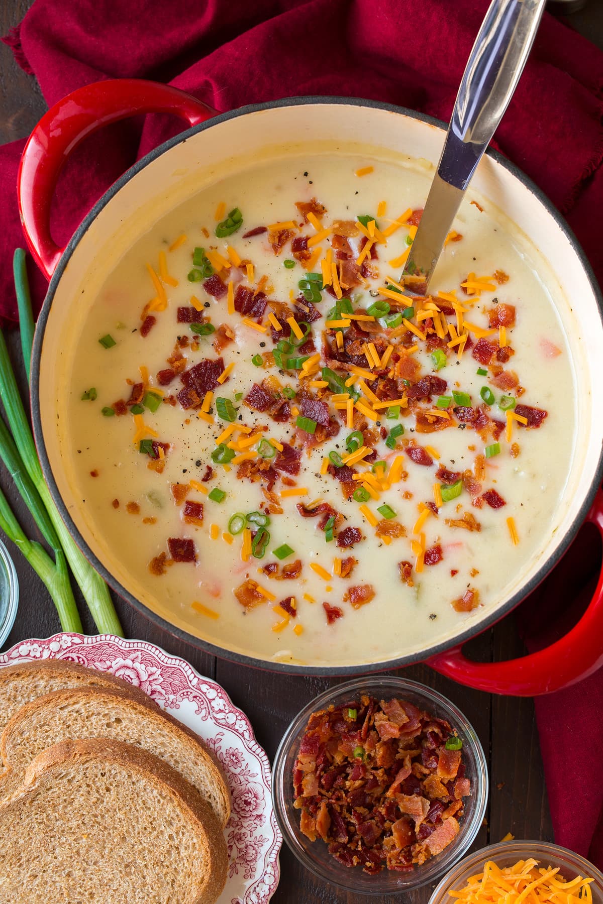 Potato Soup Overhead photo of potato soup in a large red and white pot set over a wooden tabletop with serving suggestions to the side.
