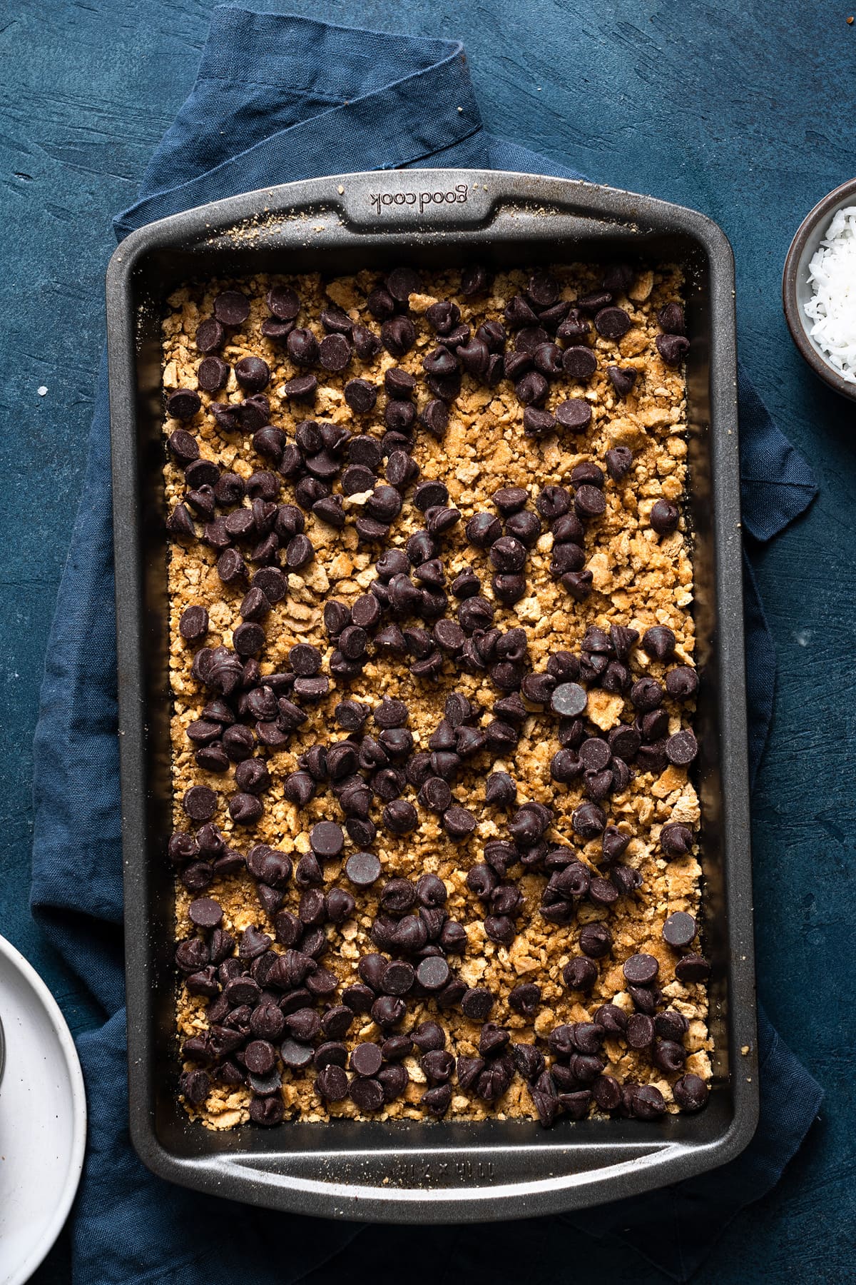 Magic Bars Showing how to make magic 7 layer bars. Sprinkling chocolate chips over graham cracker layer in baking dish.