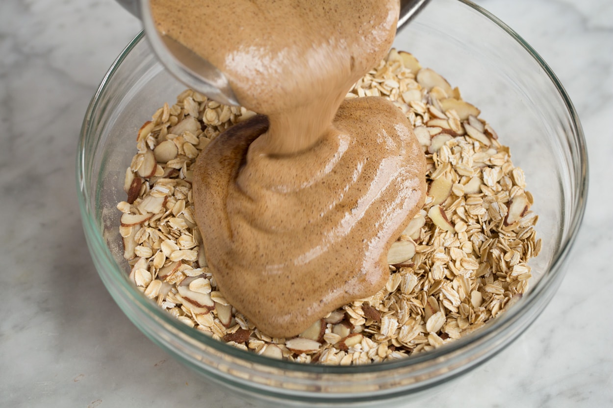 Homemade Granola Recipe Pouring honey coating over oats in mixing bowl to make granola.