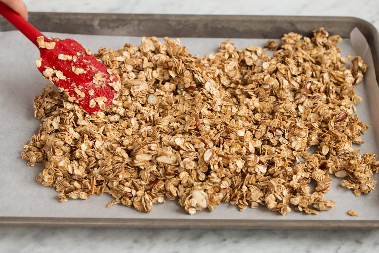 Homemade Granola Recipe Spreading granola mixture on parchment paper lined baking sheet to bake.