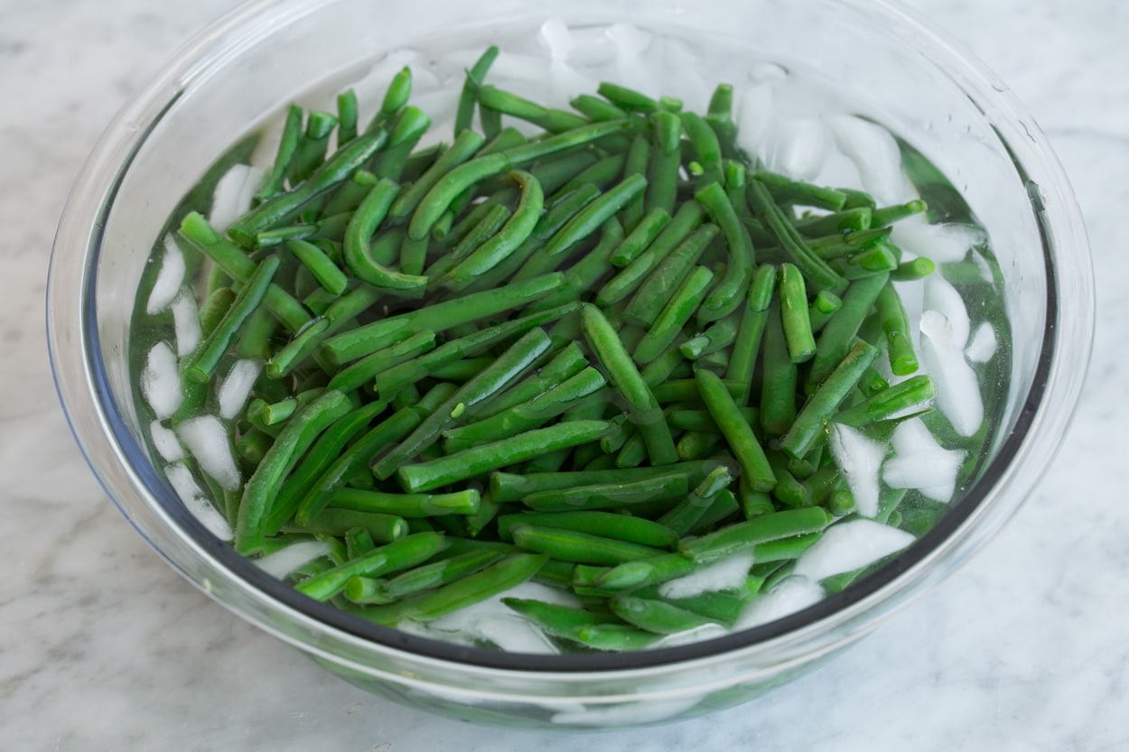 Green Bean Casserole Green beans in an ice water in a glass bowl after draining.