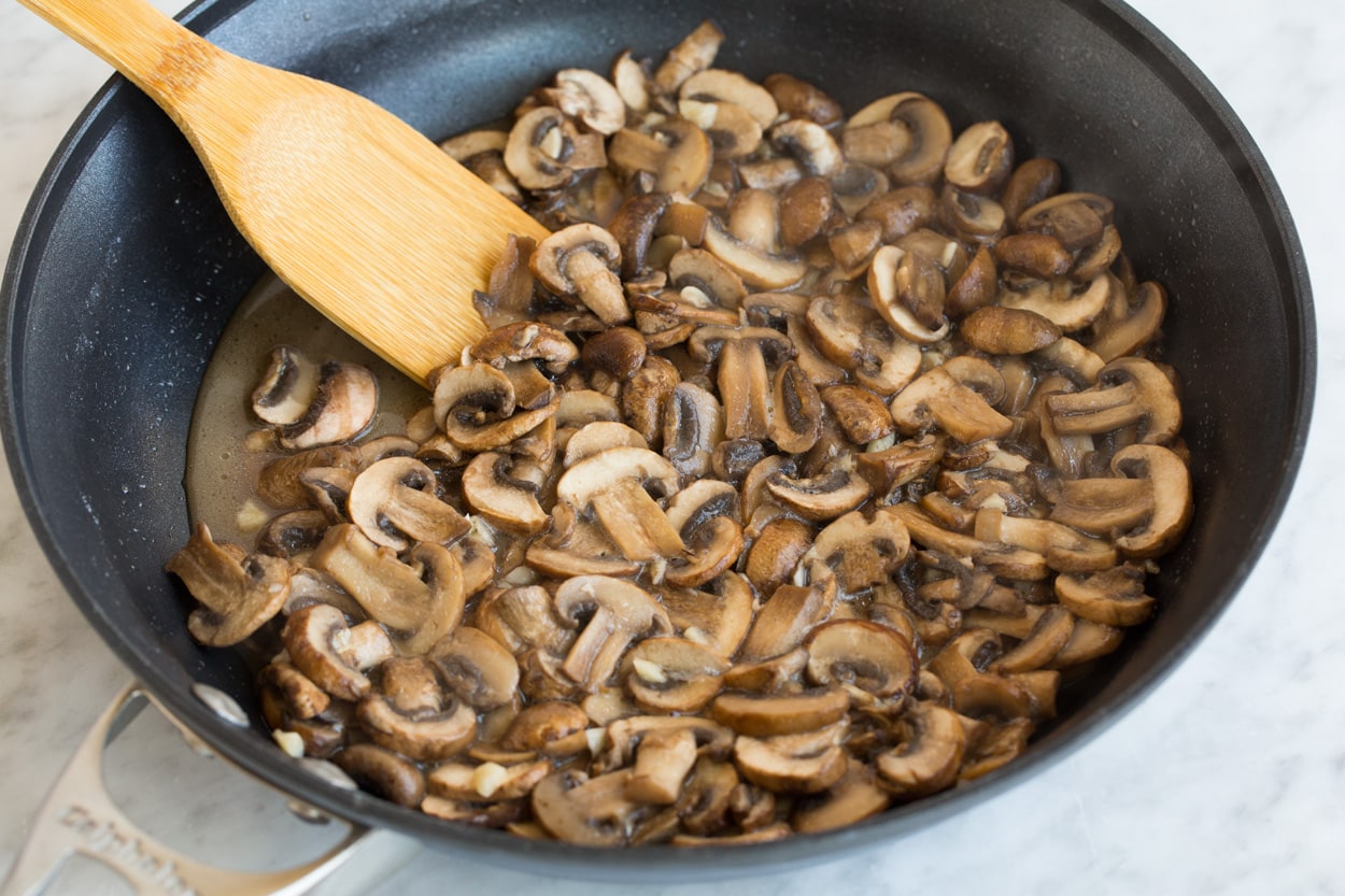 Green Bean Casserole Sauteeing mushrooms in a large dark non-stick skillet for green bean casserole.