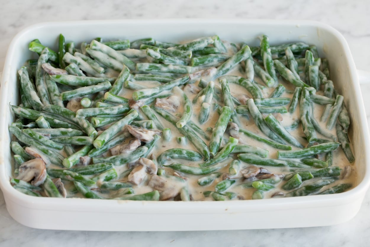 Green Bean Casserole Creamy coated green beans and mushrooms in a white ceramic baking dish before baking, for Green Bean Casserole.