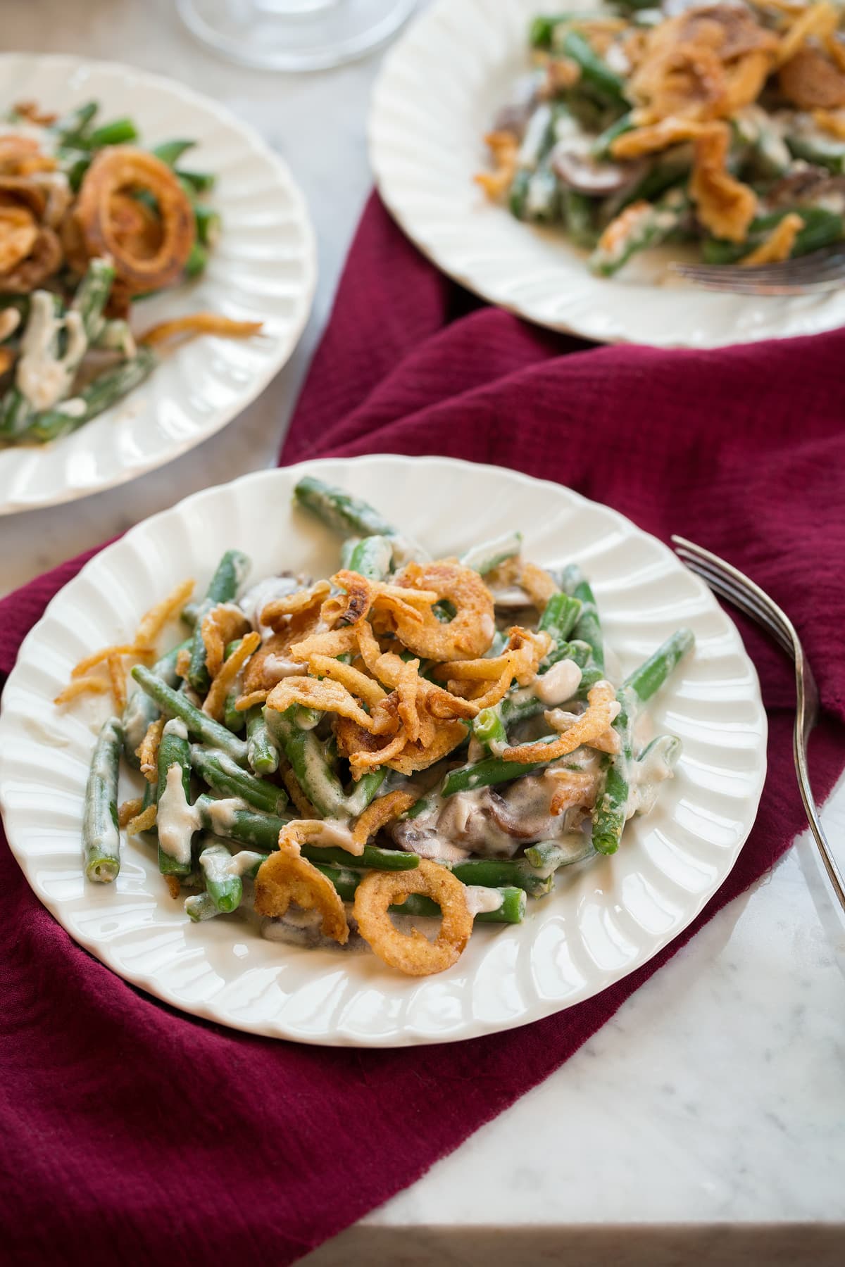 Green Bean Casserole Three individual servings of Green Bean Casserole on white scalloped salad plates.