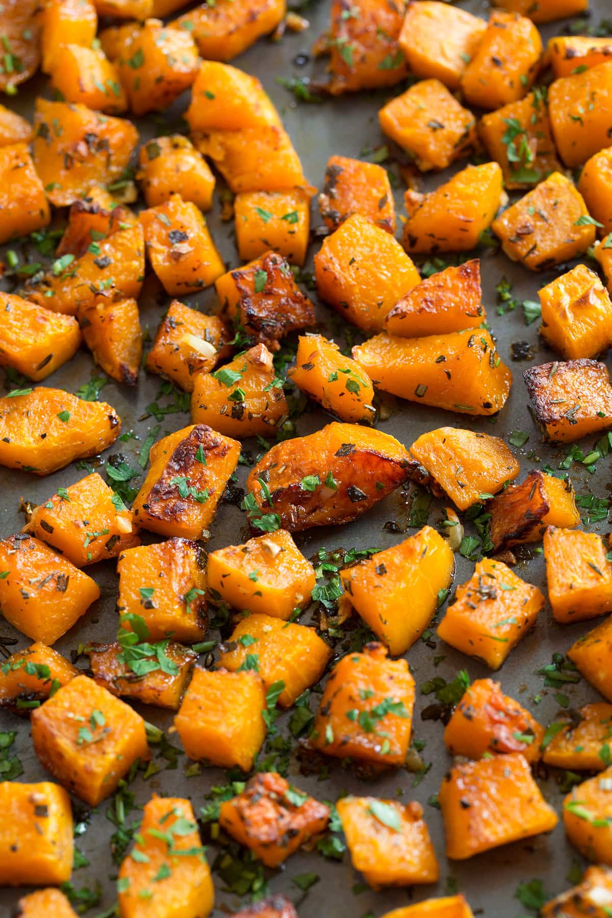 Roasted Butternut Squash with Garlic and Herbs Roasted Cubed Butternut Squash on a dark baking sheet.
