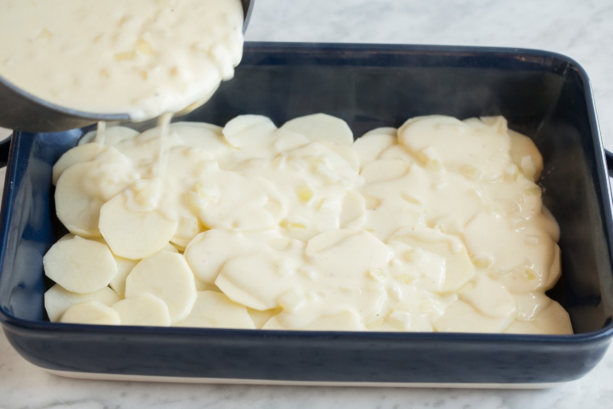 Scalloped Potatoes Pouring milk and cheese sauce over thinly sliced potatoes in a baking dish.
