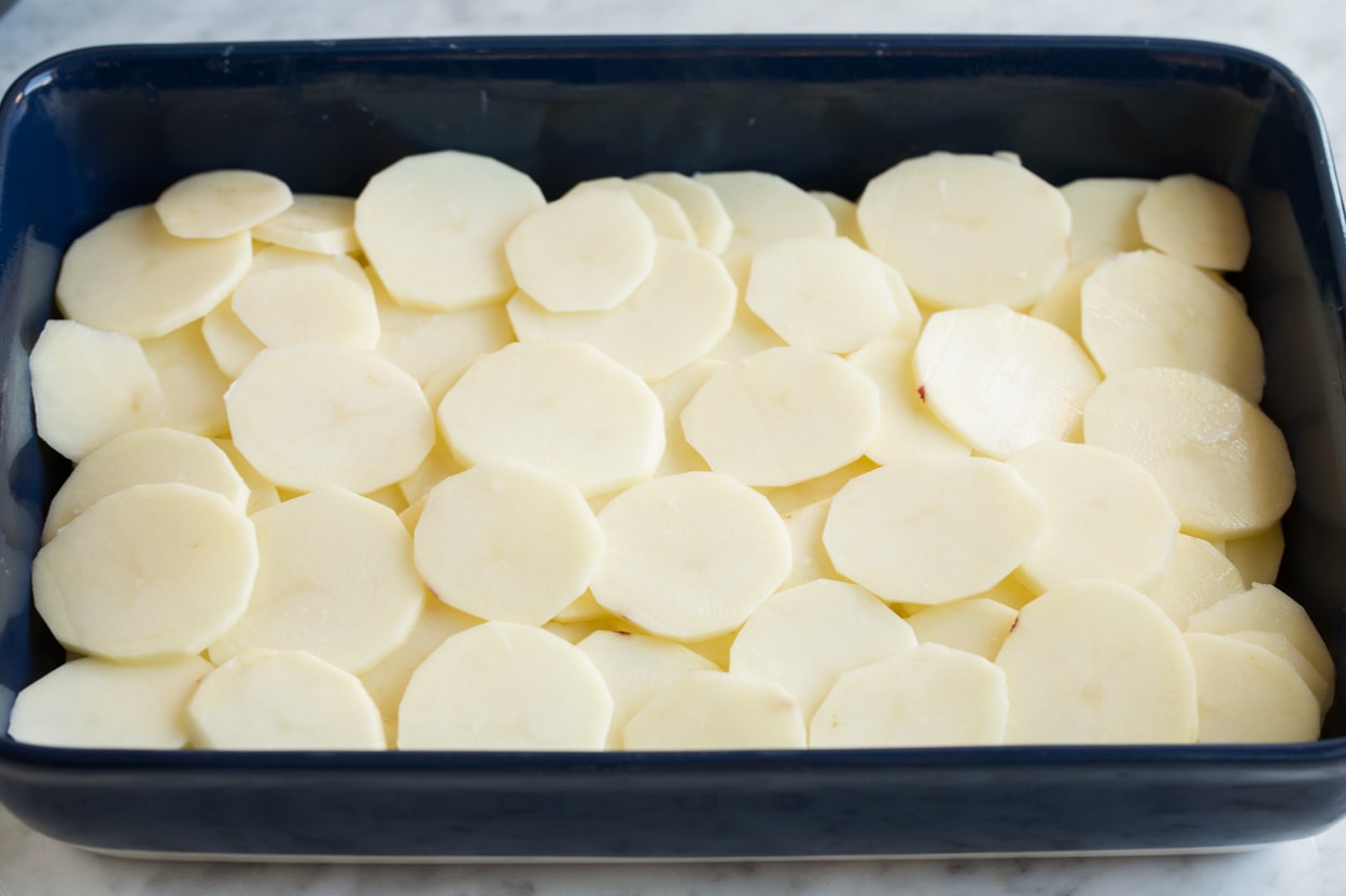 Scalloped Potatoes Spreading a second layer of thinly sliced potatoes over sauce layer in baking dish for scalloped potatoes.