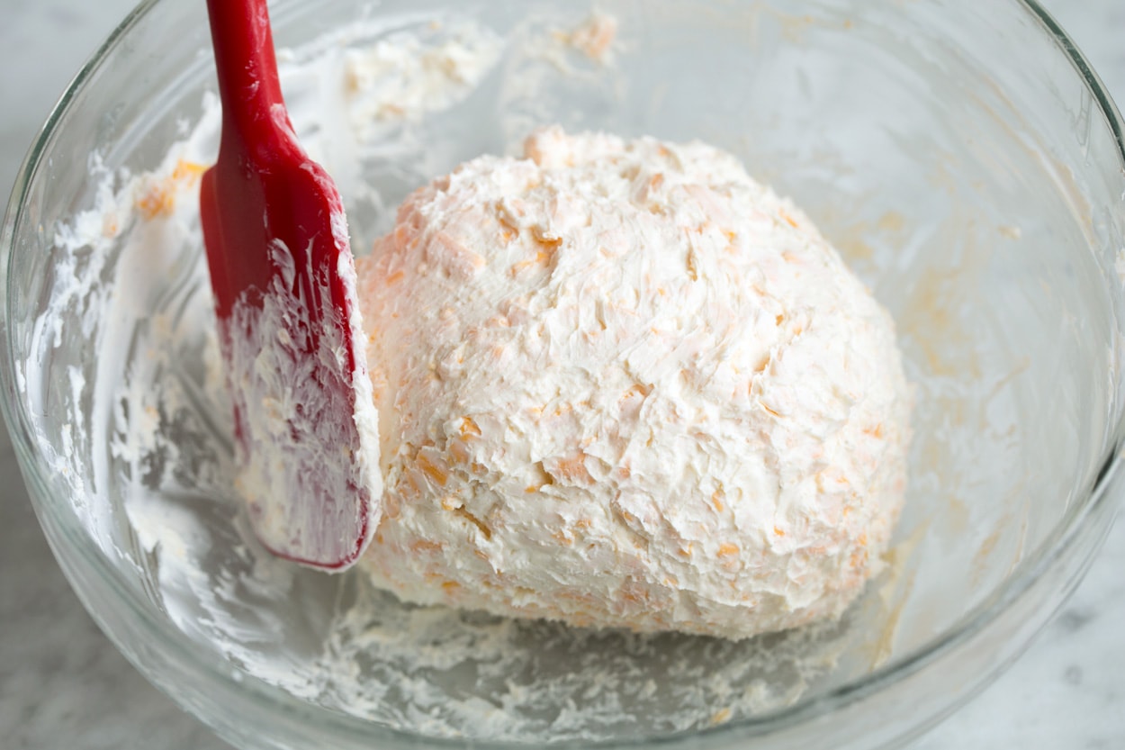 Cheese Ball Recipe Forming chilled cheese ball mixture in bowl into a ball with a spatula.