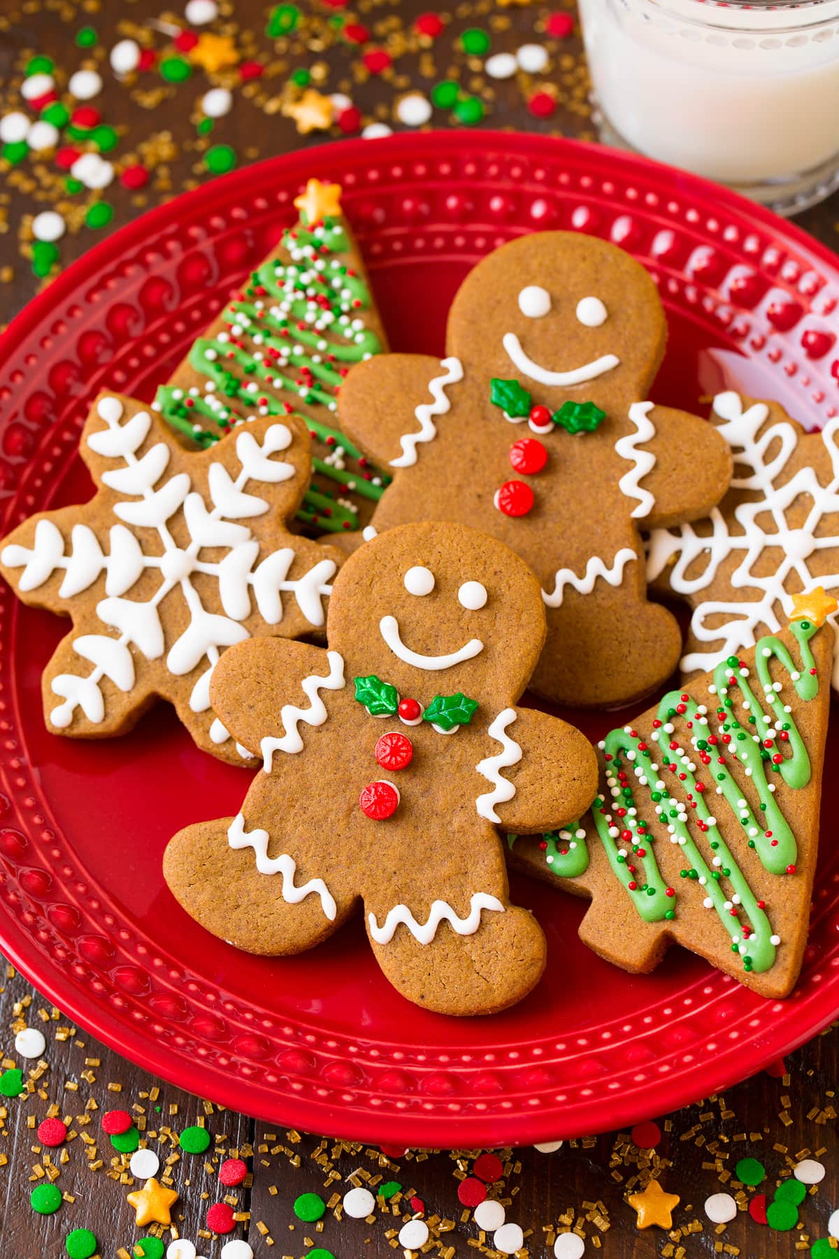 Gingerbread Cookies Gingerbread men cookies and trees and snowflakes on a red plate surrounded by Christmas sprinkles.