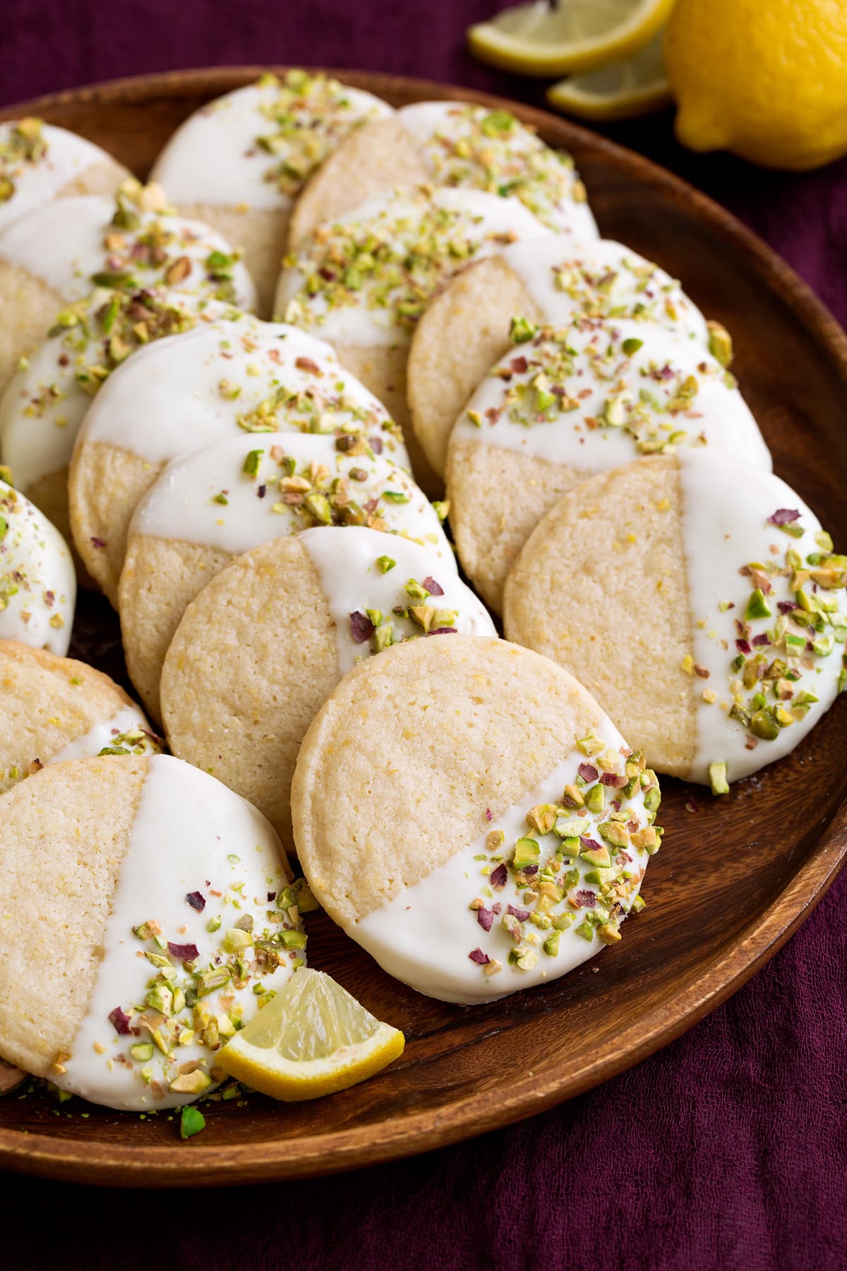 Lemon Shortbread Cookies Shortbread cookies with lemon flavor that are dipped in white chocolate and sprinkled with pistachios. Shown here on a wooden serving plate.