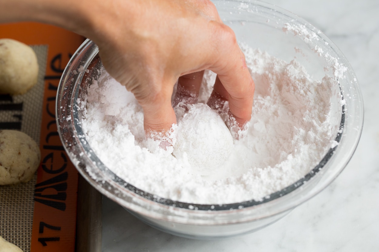 Mexican Wedding Cookies Rolling baked Mexican wedding cookies in powdered sugar after baking.