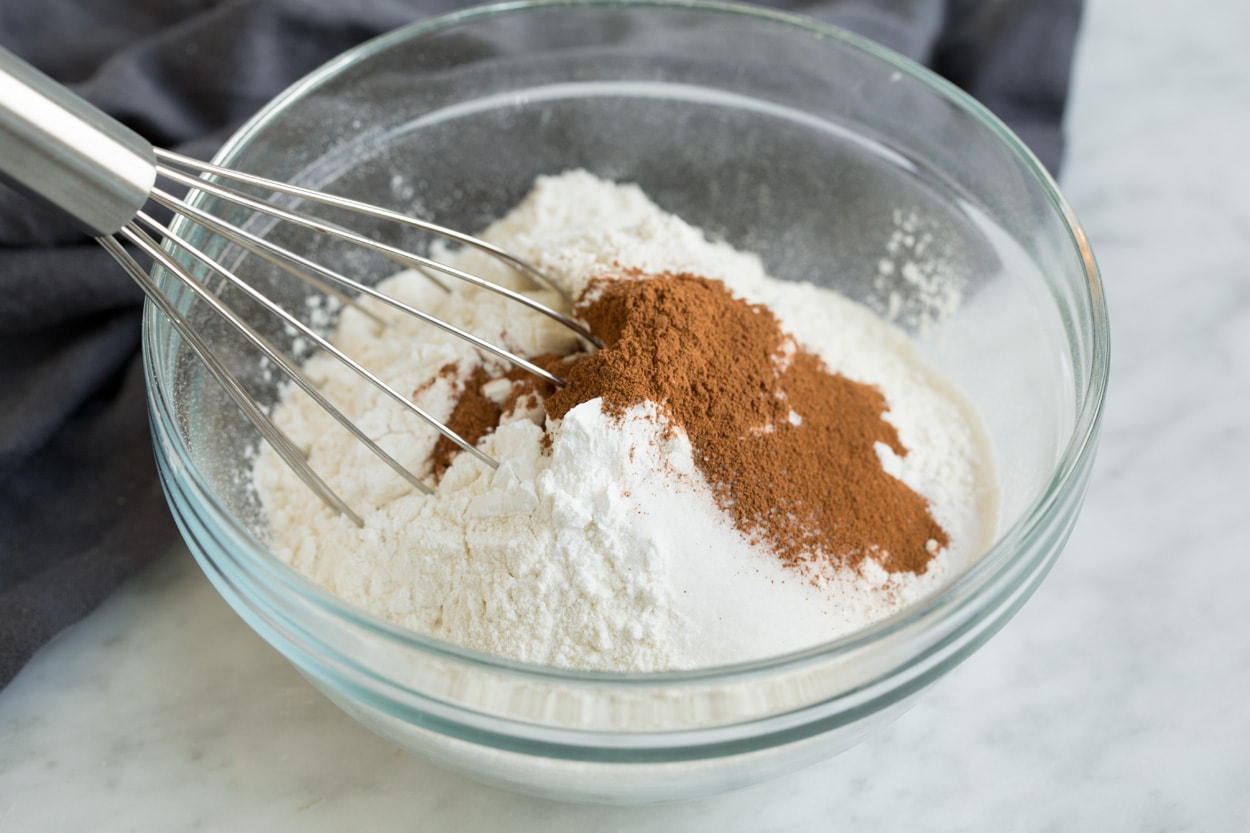 BEST Oatmeal Cookies! Showing how to make oatmeal raisin cookies. Whisking flour, cinnamon, baking soda, baking powder and salt in a glass mixing bowl.