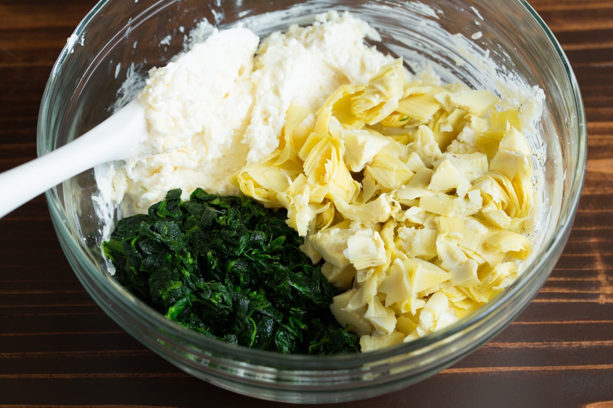 Spinach Artichoke Dip Mixing spinach and artichokes into Spinach Artichoke Dip mixture in mixing bowl.