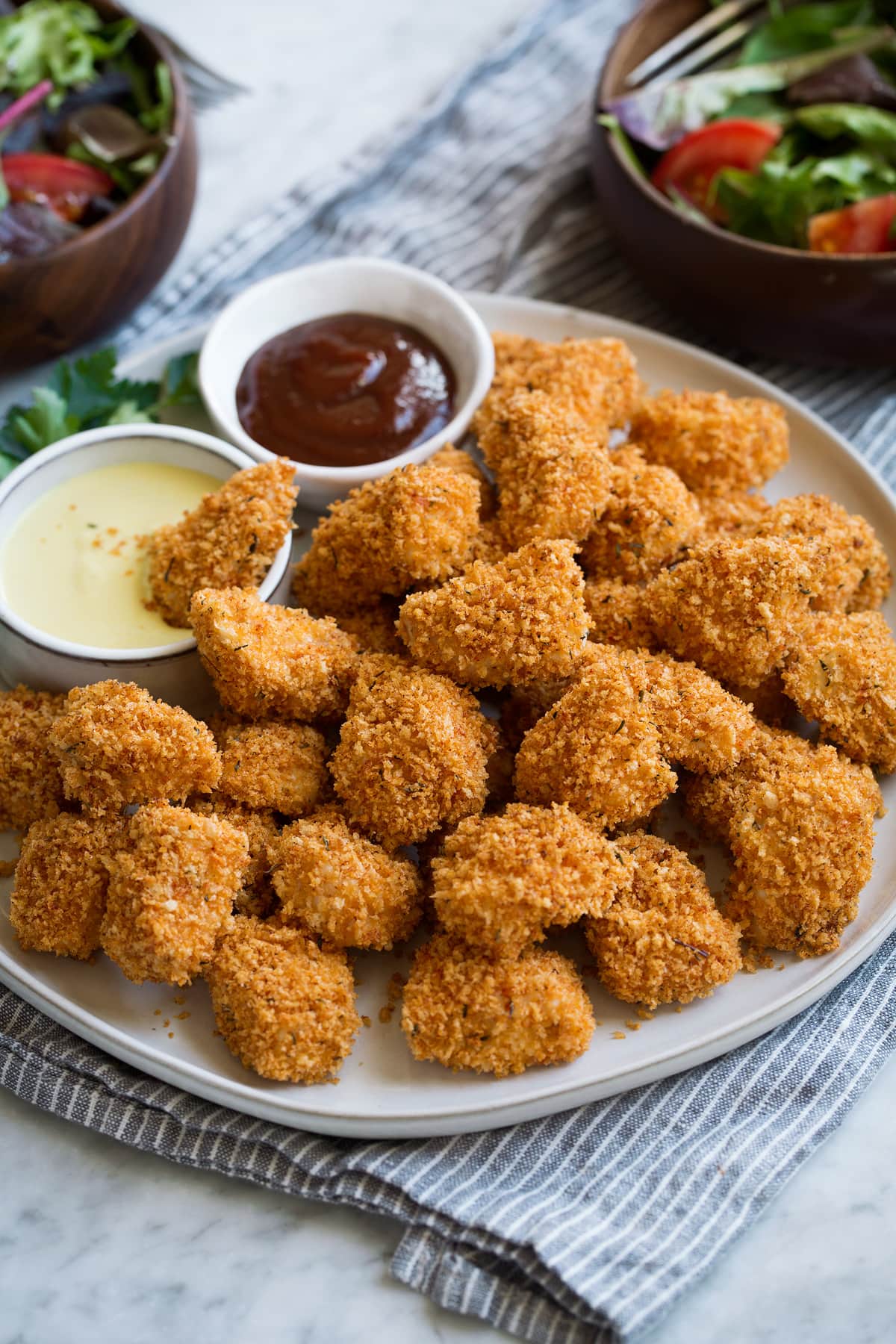Baked Chicken Nuggets Pile of chicken nuggets on a white serving platter set over a grey napkin on a marble surface.