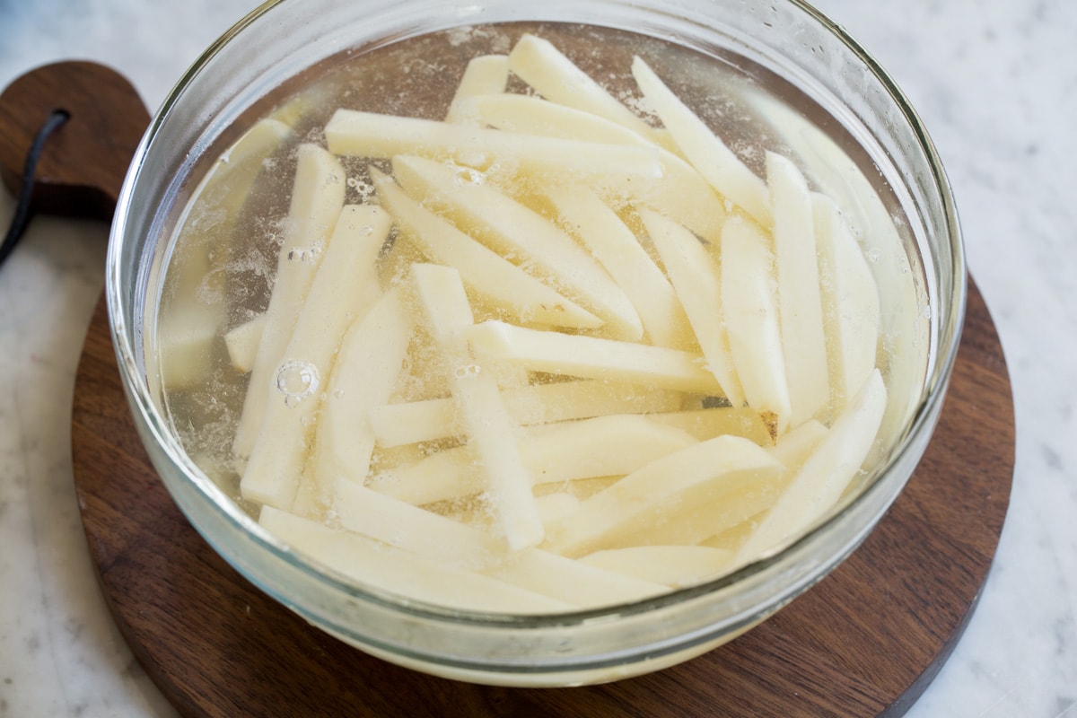 Baked French Fries Soaking potato sticks in a glass bowl full of water to remove excess starches.