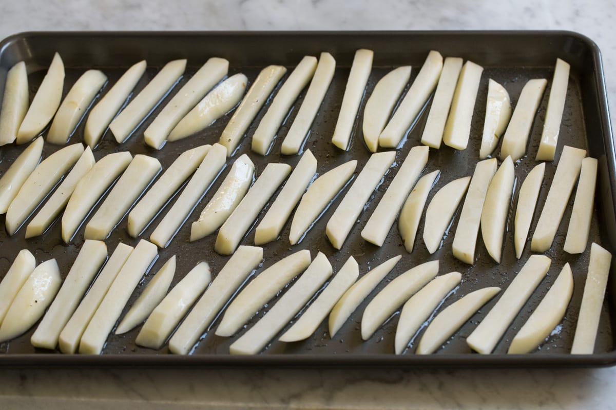 Baked French Fries Spreading cut fries onto baking sheet with oil.