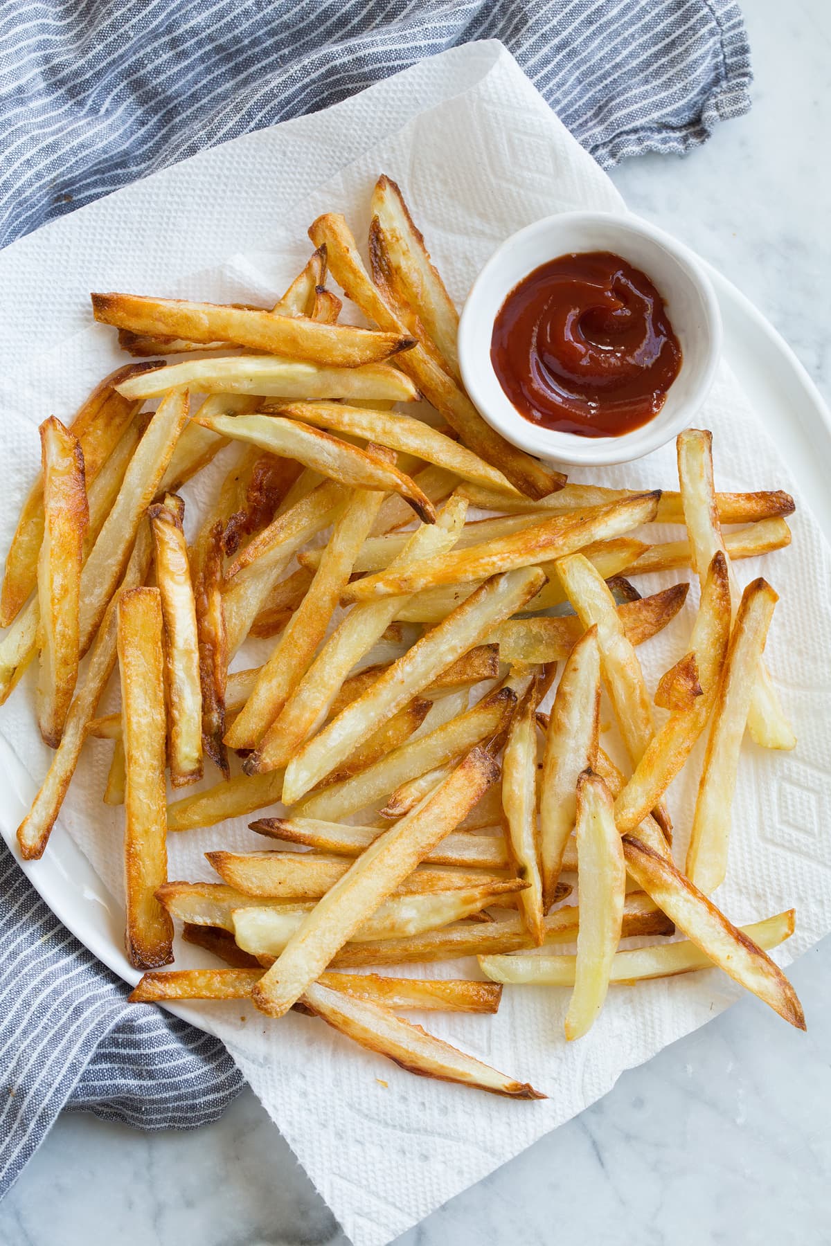 Baked French Fries - crisp exterior, fluffy interior and delicious flavor! French Fries on a napkin lined plate with a side of ketchup.