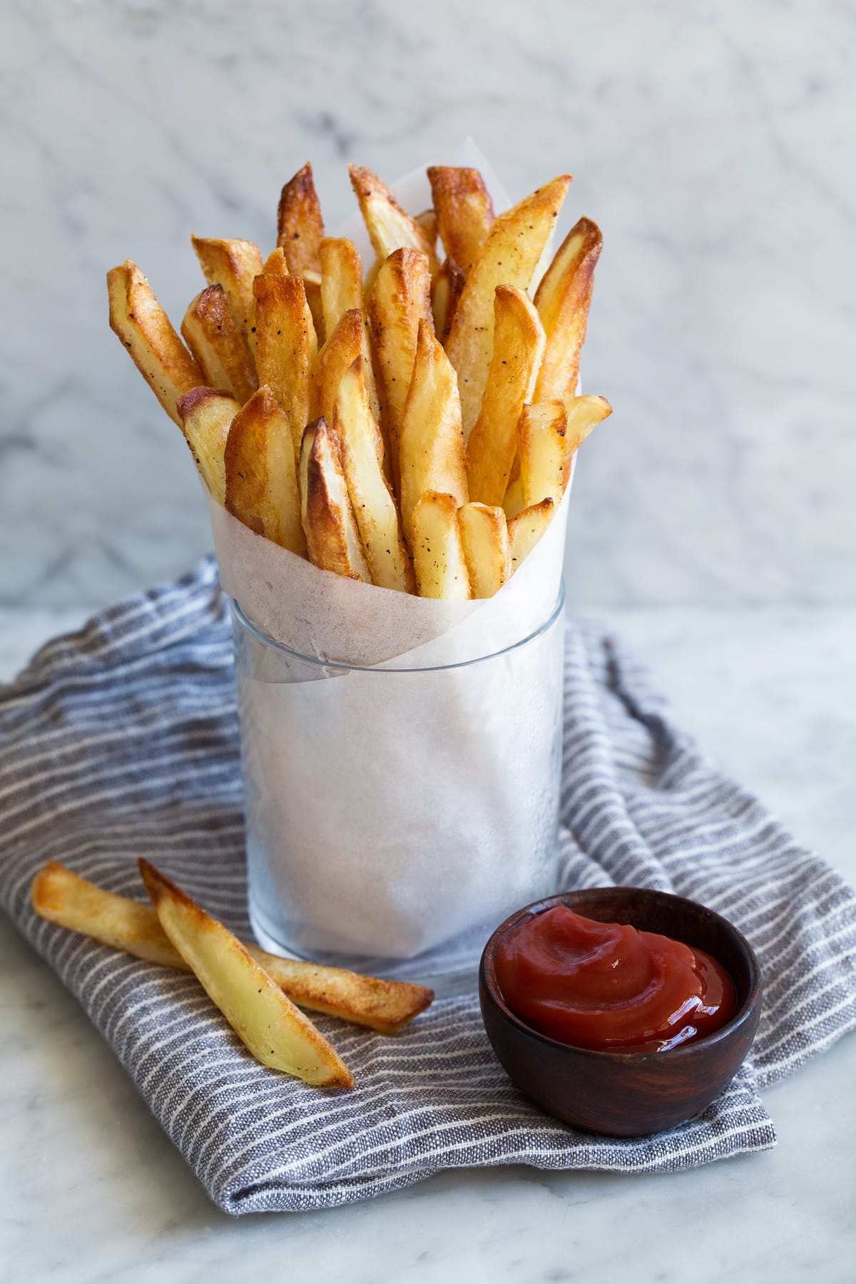 Baked French Fries - crisp exterior, fluffy interior and delicious flavor! Cup full of french fries in parchment paper with a side of ketchup.