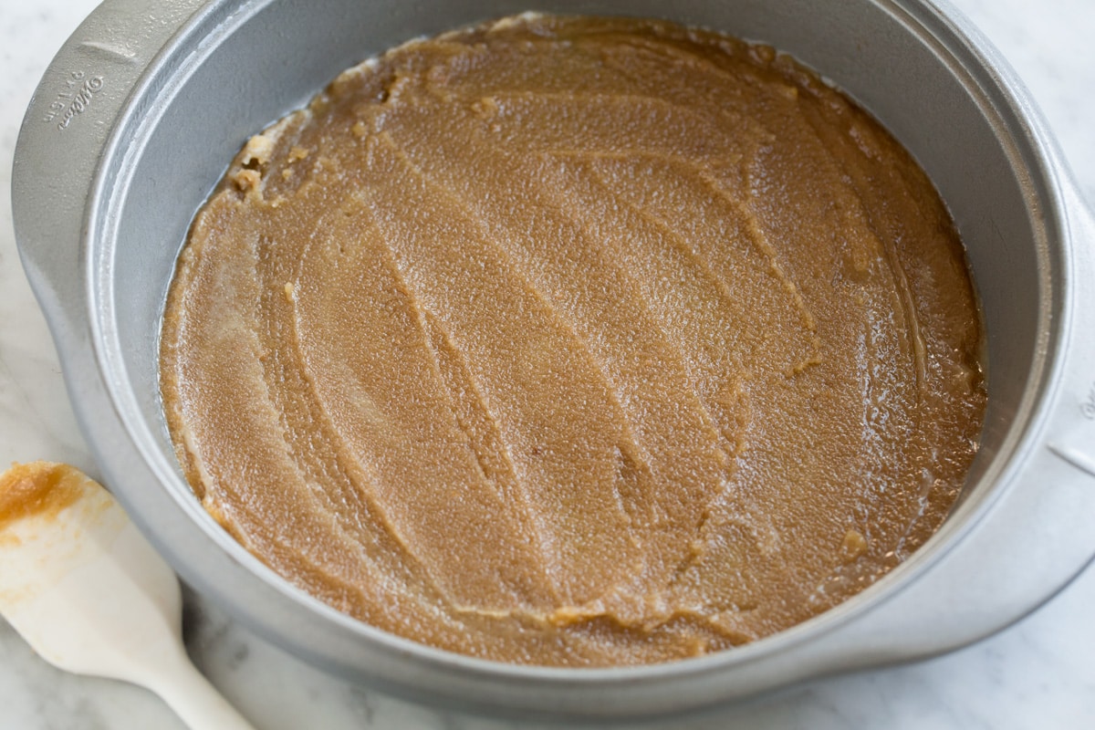 Pineapple Upside Down Cake Showing how to make Pineapple Upside Down Cake. Spreading brown sugar butter topping into a 9-inch cake pan.