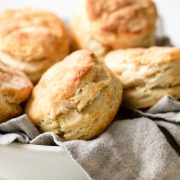 Tall and flaky biscuits stacked in a serving bowl with a grey kitchen cloth.