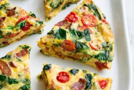 Six frittata wedges shown on a white serving platter set over a marble surface. Frittata is filled with bacon, spinach, tomatoes and swiss.