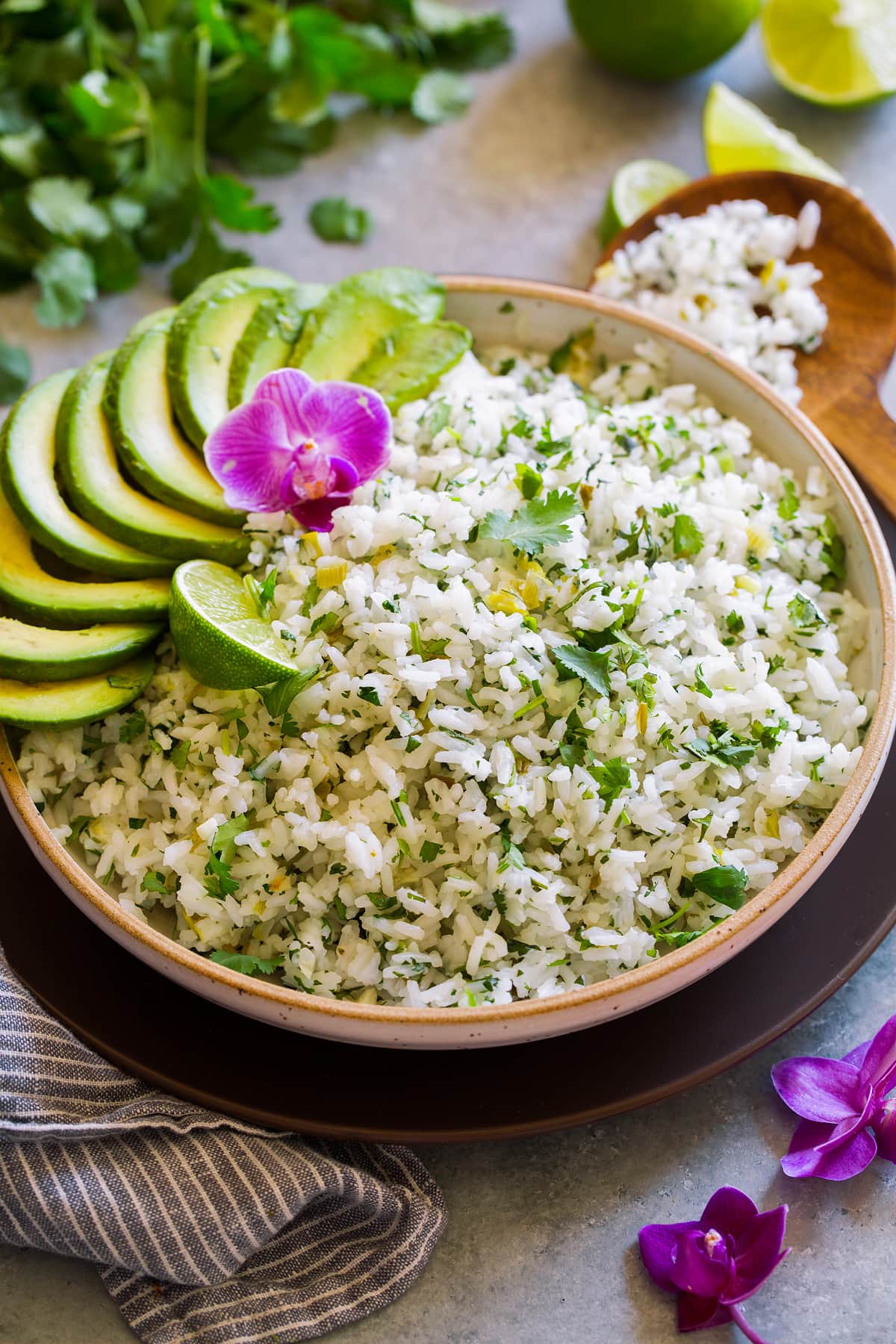 Cilantro Lime Rice Serving bowl full of cilantro lime rice garnished with avocado slices, cilantro leaves, orchid flower and lime.