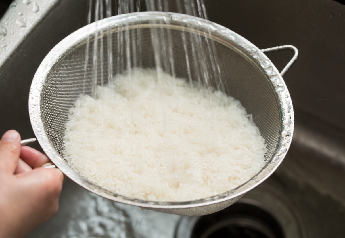 Coconut Rice Recipe Showing how to make coconut rice. Starting by rinsing rise under water in a fine mesh sieve.