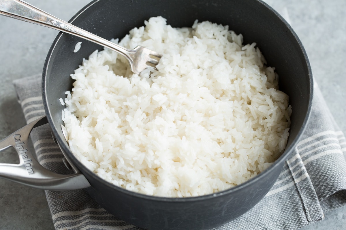 Coconut Rice Recipe Fluffing finished coconut rice in saucepan with a fork.