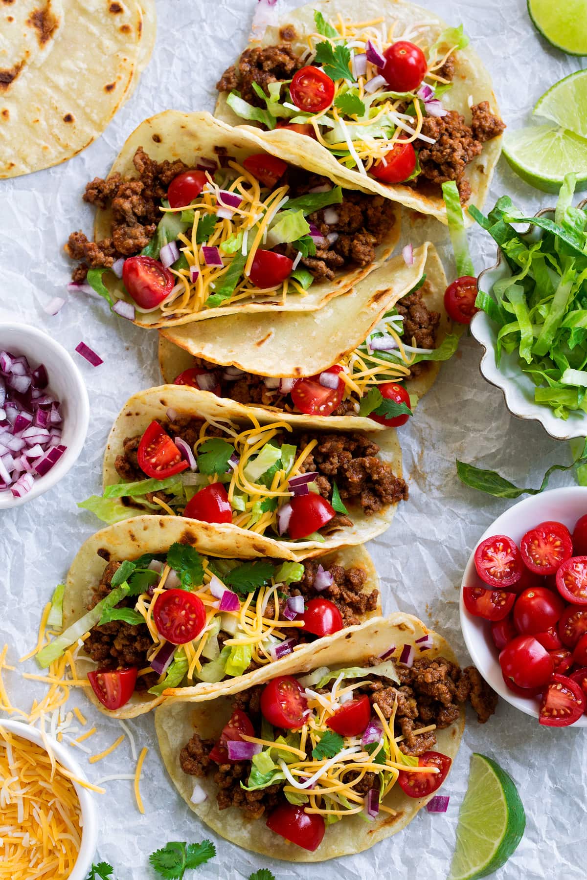 Ground Beef Tacos Long row of ground beef tacos on parchment paper finished with fresh toppings.