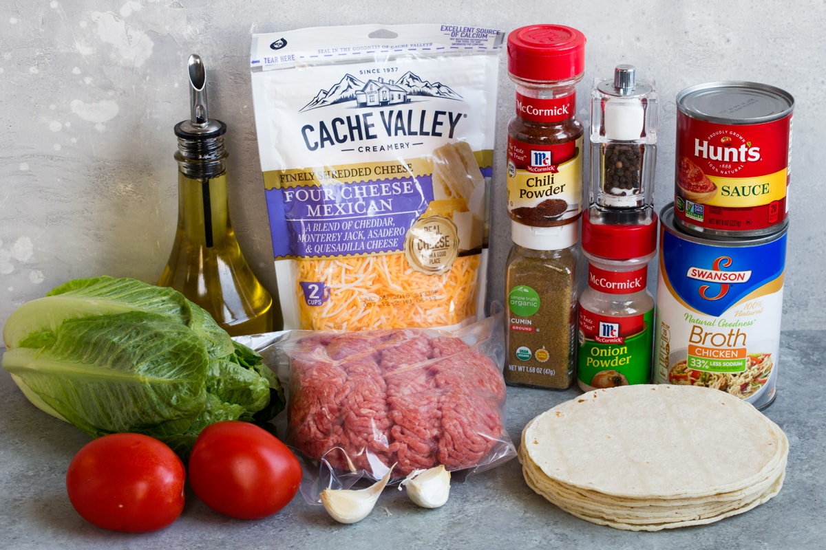 Ground Beef Tacos Ingredients needed to make tacos shown here including ground beef, oil, spices, tomato sauce, beef broth, tortillas, cheese, lettuce, garlic tomatoes.