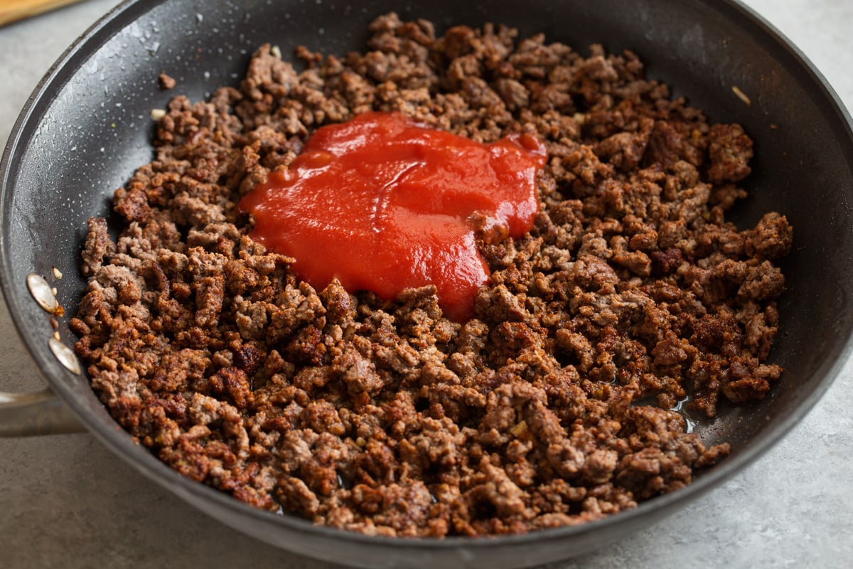 Ground Beef Tacos Adding tomato sauce and chicken broth to taco meat filling in skillet.