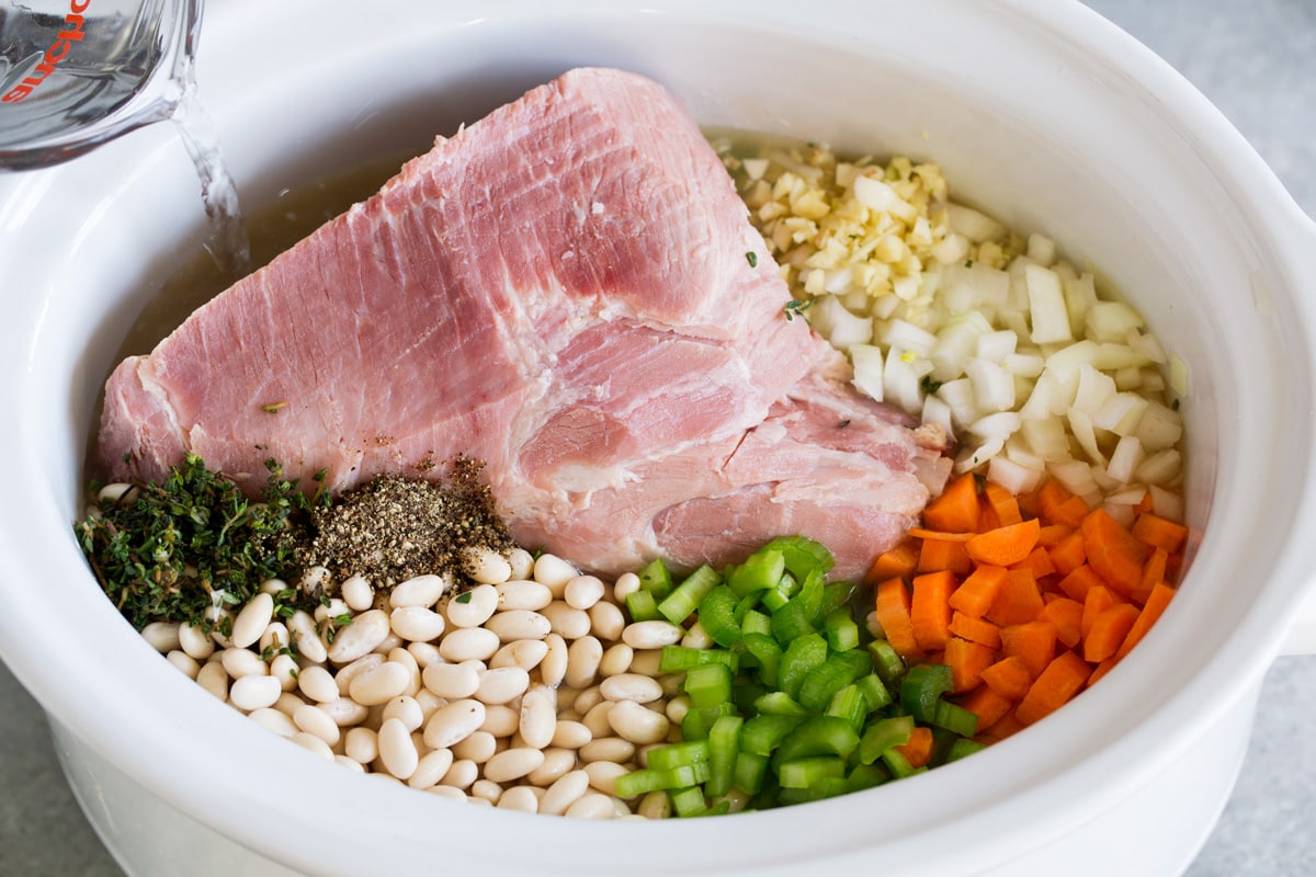 Ham and Bean Soup Showing how to make ham and bean soup. Adding all ingredients to a slow cooker including meaty ham bone, broth, garlic, onion, carrots, celery, great northern beans, thyme and pepper.