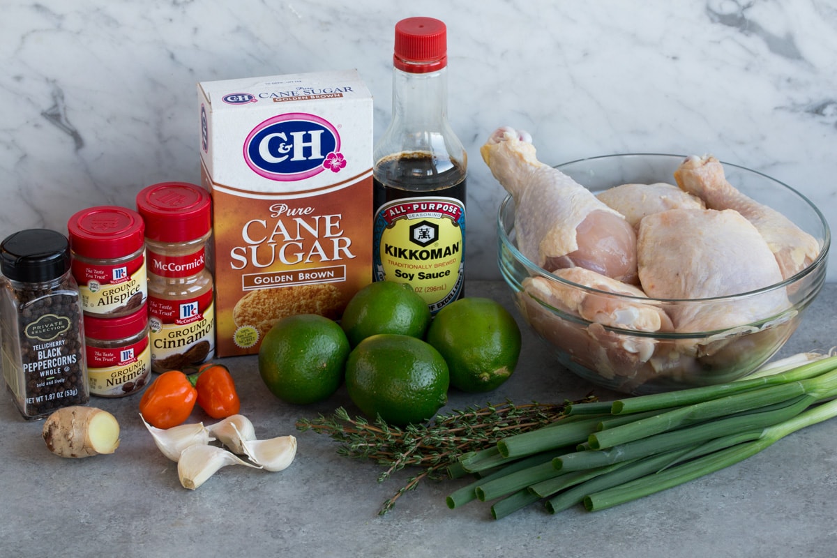 Perfect Jerk Chicken Jerk Chicken ingredients shown here including chicken pieces, green onions, thyme, limes, soy sauce, brown sugar, cinnamon, allspice, nutmeg, pepper, scotch bonnet pepper, garlic, and fresh ginger.