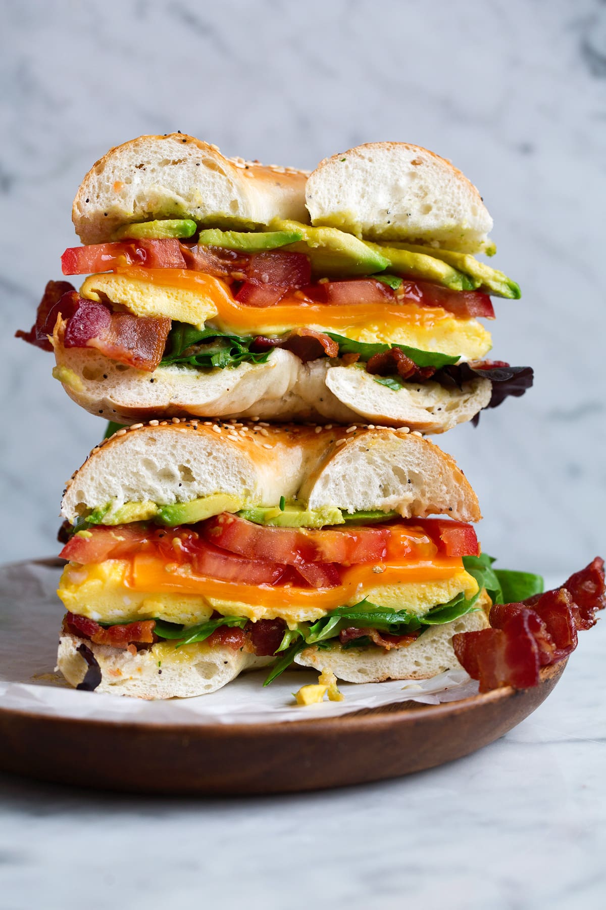 Microwave Scrambled Eggs - super fast, super easy and always delicious! Perfect for breakfast sandwiches too! #eggs #breakfast #easybreakfast #quickbreakfast Bagel sandwich with microwave eggs, bacon, avocado, tomato, cheddar and lettuce. Sandwich is cut in half and stacked on a wooden plate set over a marble surface.