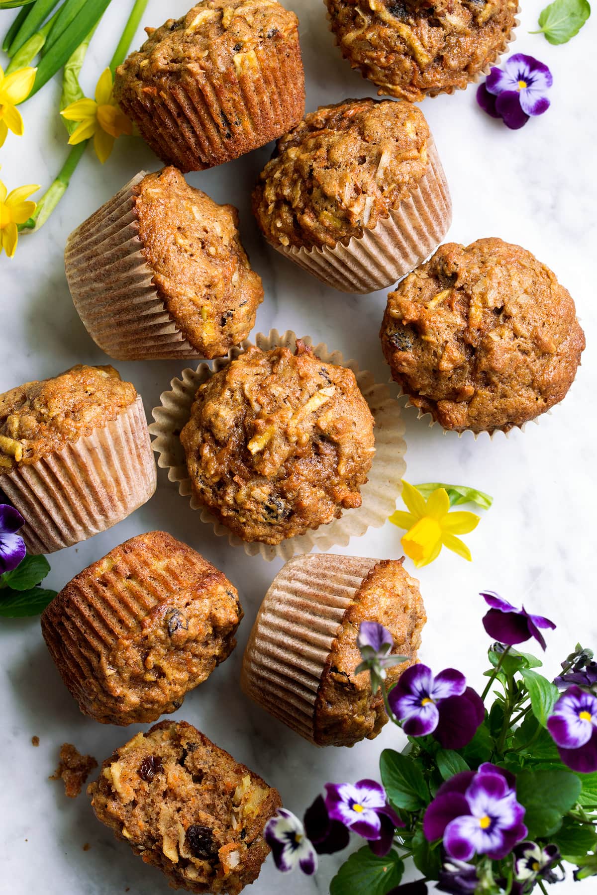Morning Glory Muffins Overhead image of morning glory muffins on a marble surface decorated with spring flowers.