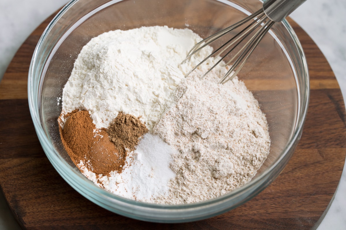 Morning Glory Muffins Showing how to make morning glory muffins. Whisking white flour, wheat flour, cinnamon, nutmeg, baking soda and salt in a glass mixing bowl.