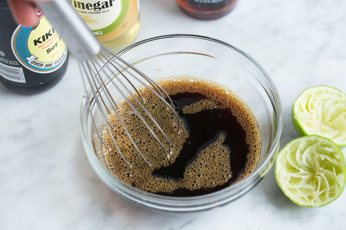 Pad Thai (with Chicken or Shrimp) Showing how to make pad thai sauce. Whisking soy sauce, fish sauce, lime juice, rice vinegar and brown sugar in a glass mixing bowl set over a marble surface.