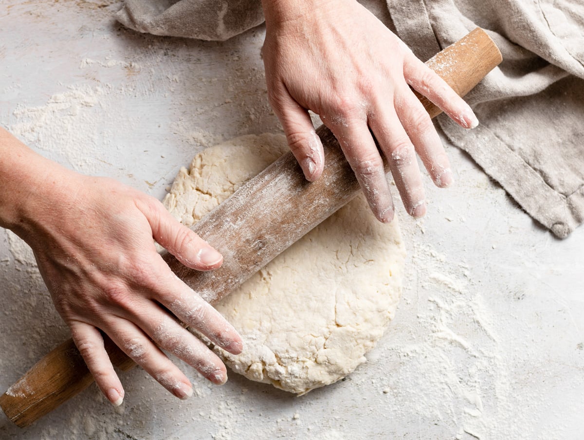 Homemade Buttermilk Biscuits Gently rolling biscuit dough out using a rolling pin on a floured surface.