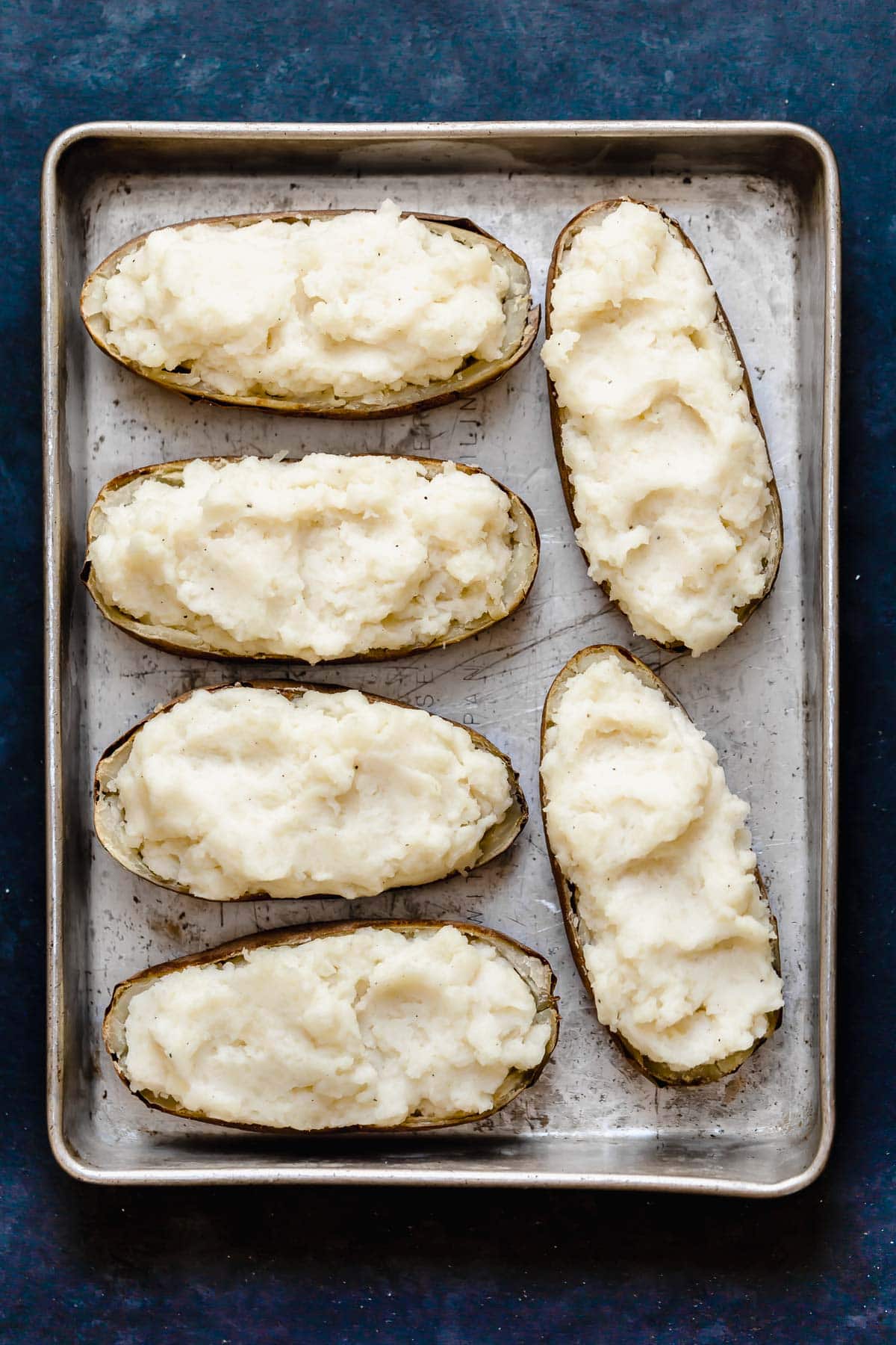 Twice Baked Potatoes Six potato skins filled with mashed potatoes sitting on a metal baking dish.