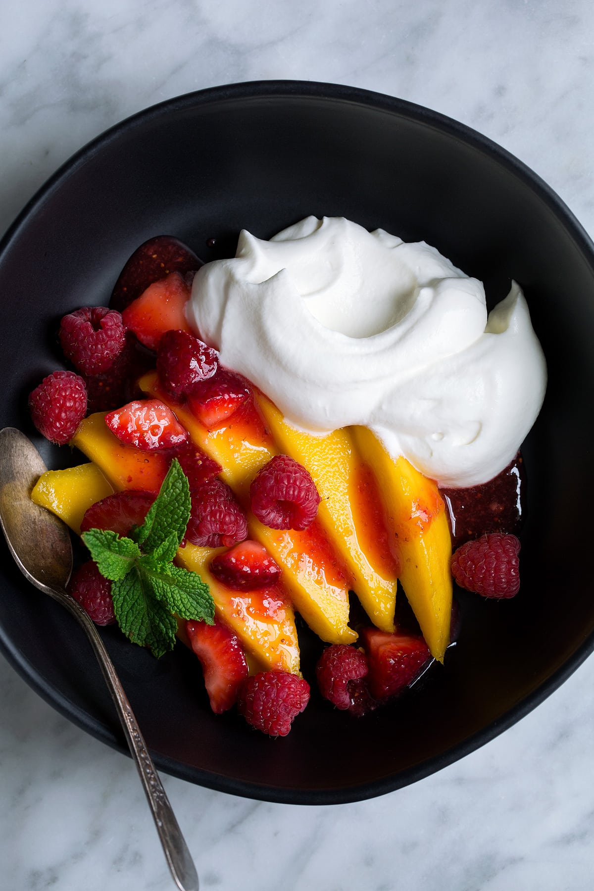 How to Make Whipped Cream Whipped Cream served with fresh mangoes, strawberries and raspberries in a black bowl.